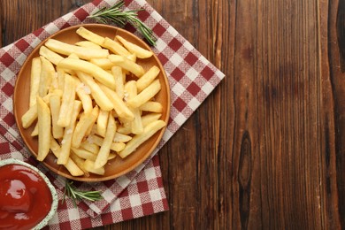 Photo of Tasty french fries served with ketchup and rosemary on wooden table, top view. Space for text