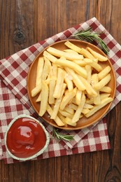 Photo of Tasty french fries served with ketchup and rosemary on wooden table, top view