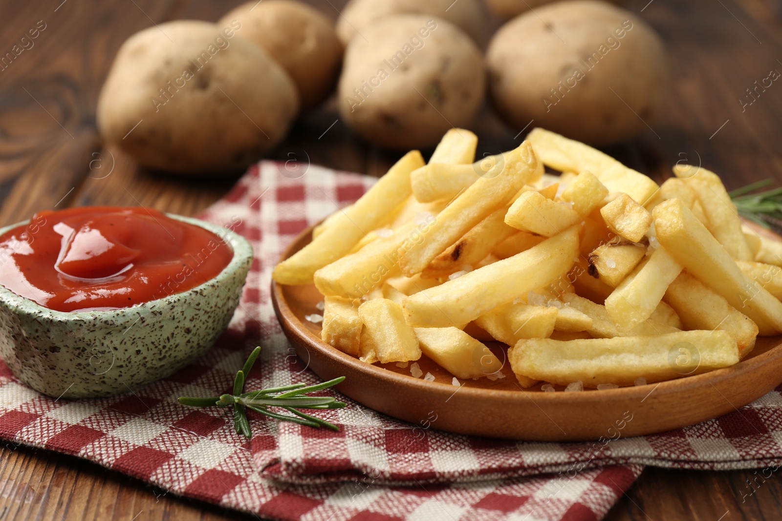 Tasty french fries served with ketchup and rosemary on wooden table, closeup Photo of Tasty french fries served with ketchup and rosemary on wooden table, closeup