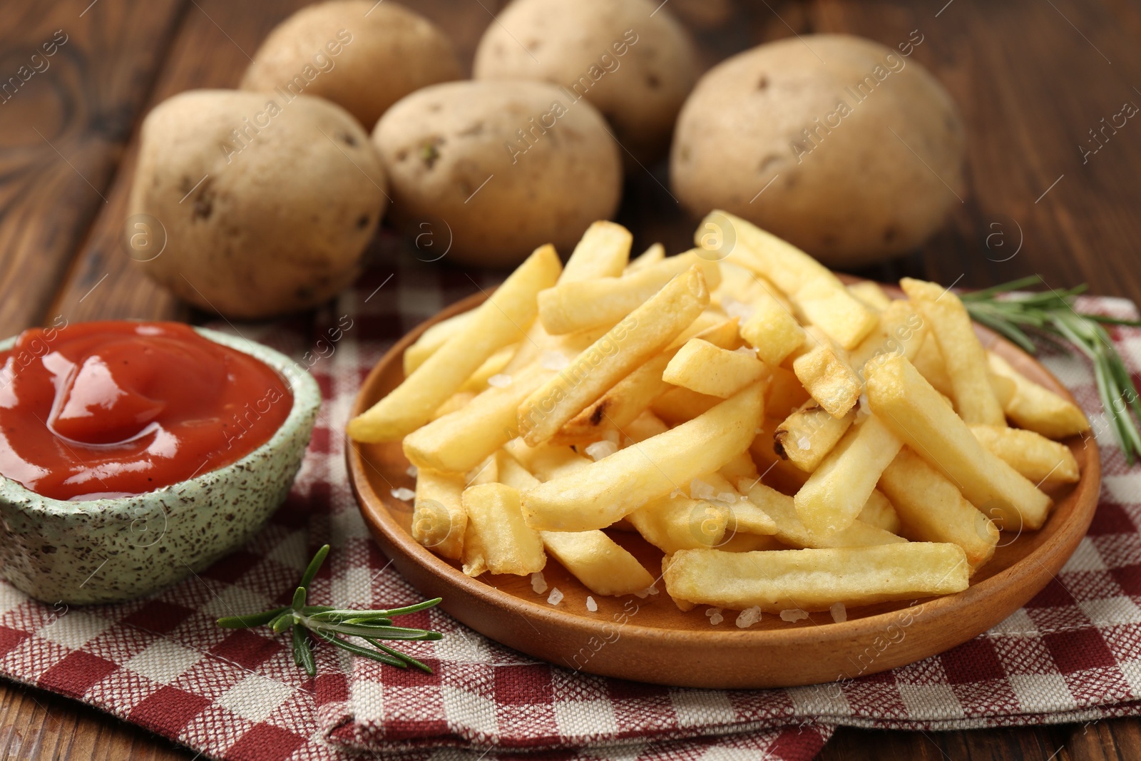 Tasty french fries served with ketchup and rosemary on wooden table, closeup Photo of Tasty french fries served with ketchup and rosemary on wooden table, closeup