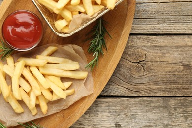 Photo of Tasty french fries served with ketchup and rosemary on wooden table, top view. Space for text