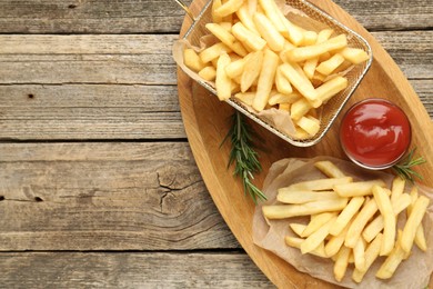 Photo of Tasty french fries served with ketchup and rosemary on wooden table, top view. Space for text