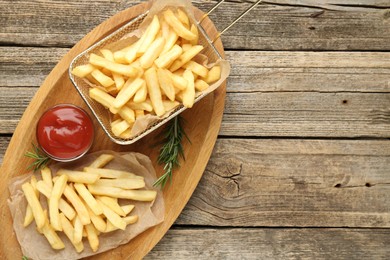 Photo of Tasty french fries served with ketchup and rosemary on wooden table, top view. Space for text