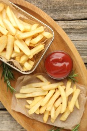 Photo of Tasty french fries served with ketchup and rosemary on wooden table, top view