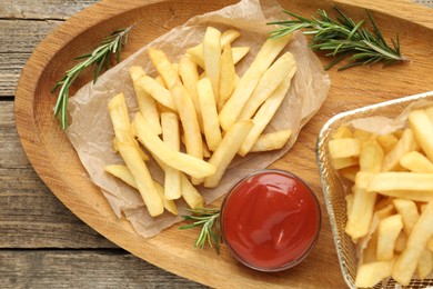 Photo of Tasty french fries served with ketchup and rosemary on wooden table, top view