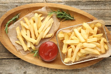 Photo of Tasty french fries served with ketchup and rosemary on wooden table, top view