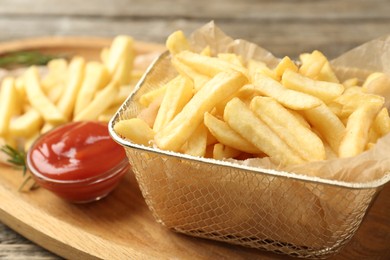 Photo of Tasty french fries served with ketchup and rosemary on wooden table, closeup