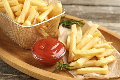 Photo of Tasty french fries served with ketchup and rosemary on wooden table, closeup