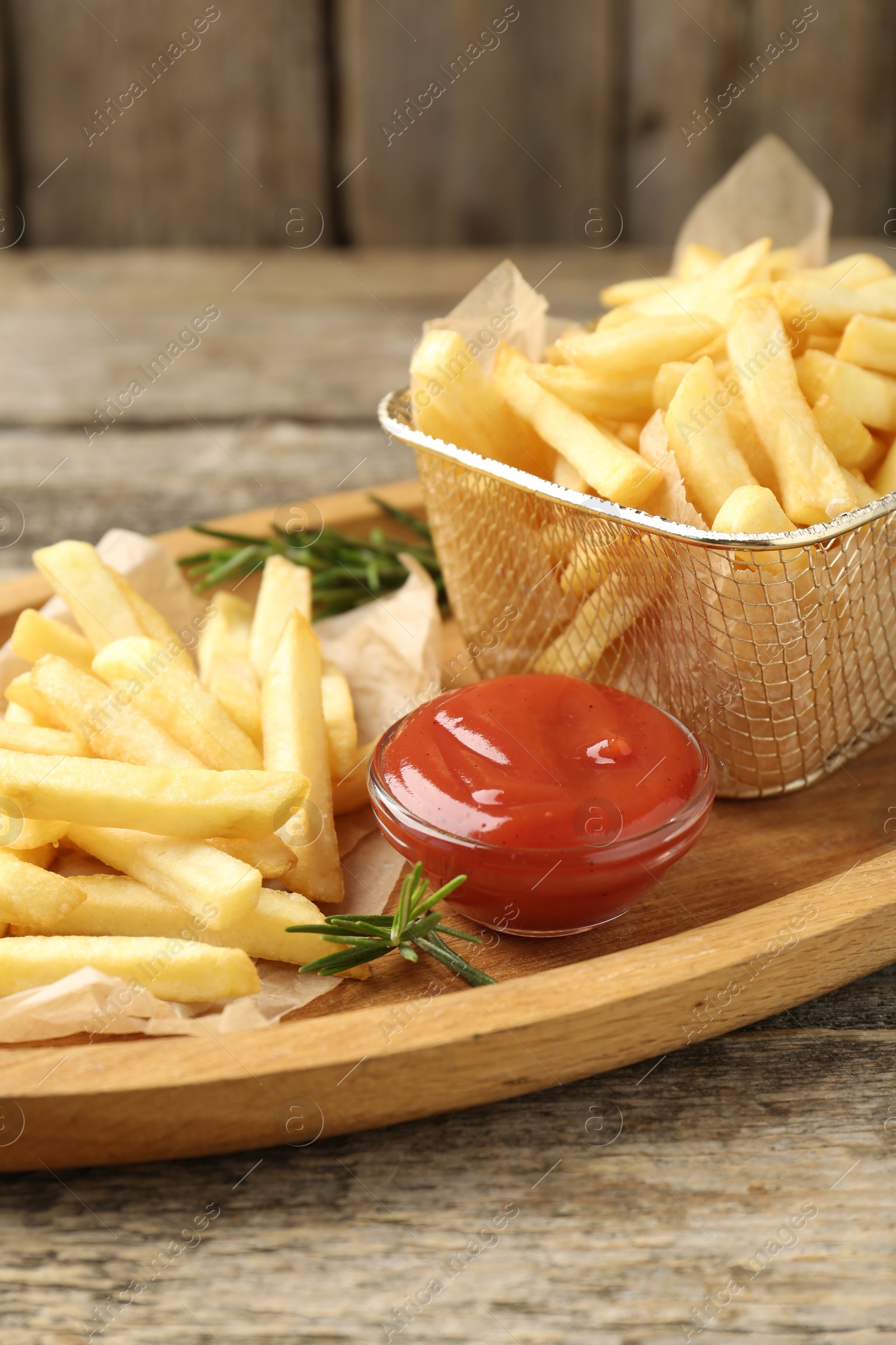 Tasty french fries served with ketchup and rosemary on wooden table, closeup Photo of Tasty french fries served with ketchup and rosemary on wooden table, closeup
