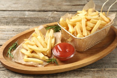 Photo of Tasty french fries served with ketchup and rosemary on wooden table, closeup