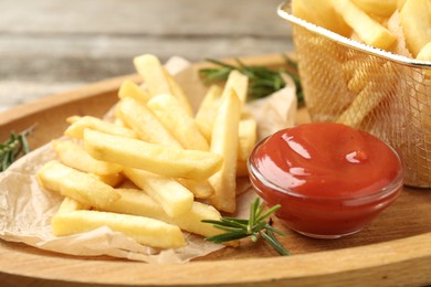 Photo of Tasty french fries served with ketchup and rosemary on wooden table, closeup
