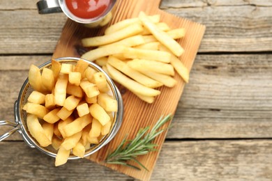 Photo of Tasty french fries served with ketchup and rosemary on wooden table, top view. Space for text