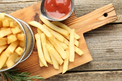 Photo of Tasty french fries served with ketchup and rosemary on wooden table, top view