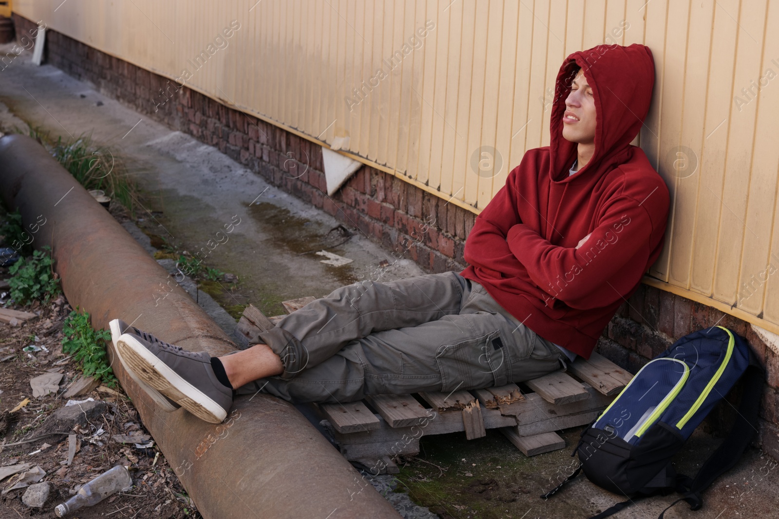Homeless man sitting near yellow wall on city street Photo of Homeless man sitting near yellow wall on city street