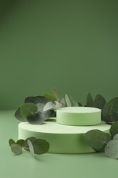 Photo of Beautiful eucalyptus branches on podium against green background. Space for text