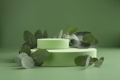 Photo of Beautiful eucalyptus branches on podium against green background. Space for text