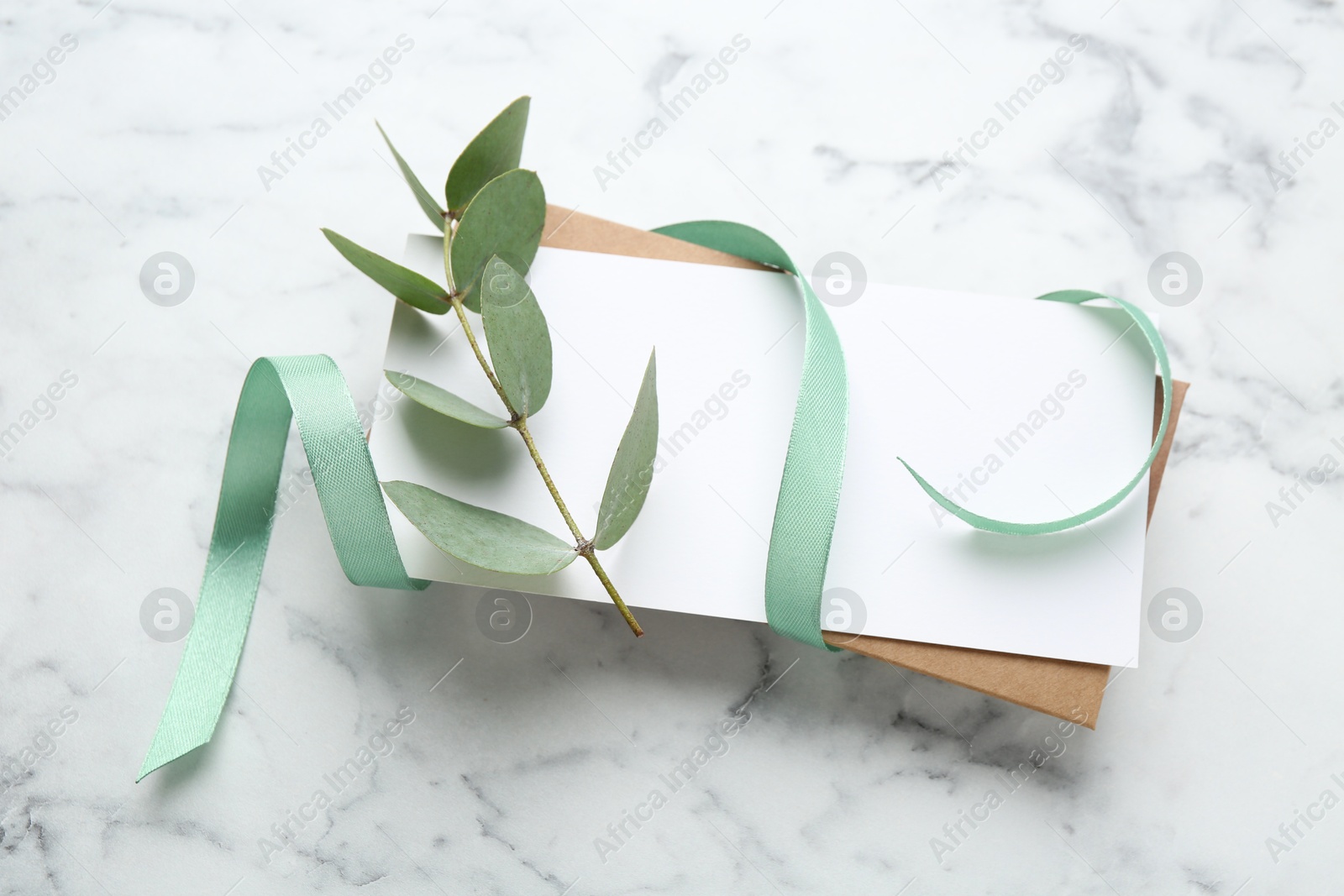 Blank card, ribbon and eucalyptus branch on white marble background, flat lay Photo of Blank card, ribbon and eucalyptus branch on white marble background, flat lay