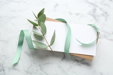 Photo of Blank card, ribbon and eucalyptus branch on white marble background, flat lay