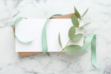 Photo of Blank card, ribbon and eucalyptus branch on white marble background, flat lay