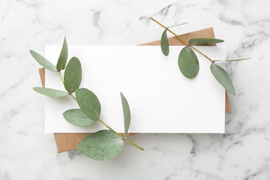 Photo of Blank card and eucalyptus branches on white marble background, flat lay