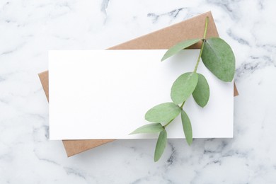 Photo of Blank card and eucalyptus branch on white marble background, flat lay