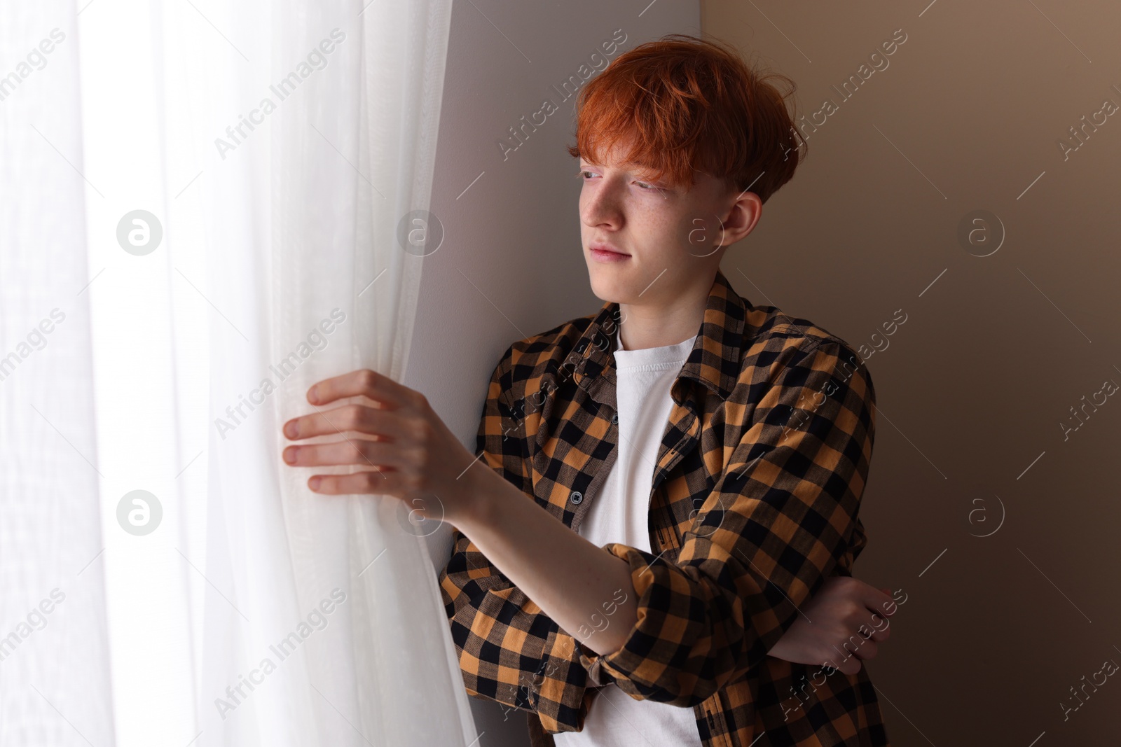 Teen problems. Depressed teenage boy looking out window indoors Photo of Teen problems. Depressed teenage boy looking out window indoors