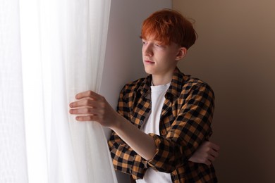 Photo of Teen problems. Depressed teenage boy looking out window indoors
