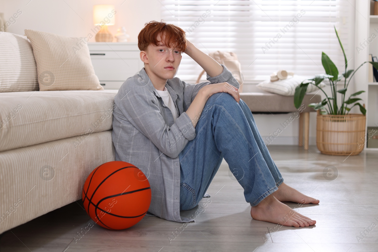 Teen problems. Depressed teenage boy with basketball ball on floor indoors Photo of Teen problems. Depressed teenage boy with basketball ball on floor indoors