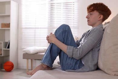 Photo of Teen problems. Depressed teenage boy on sofa at home, space for text
