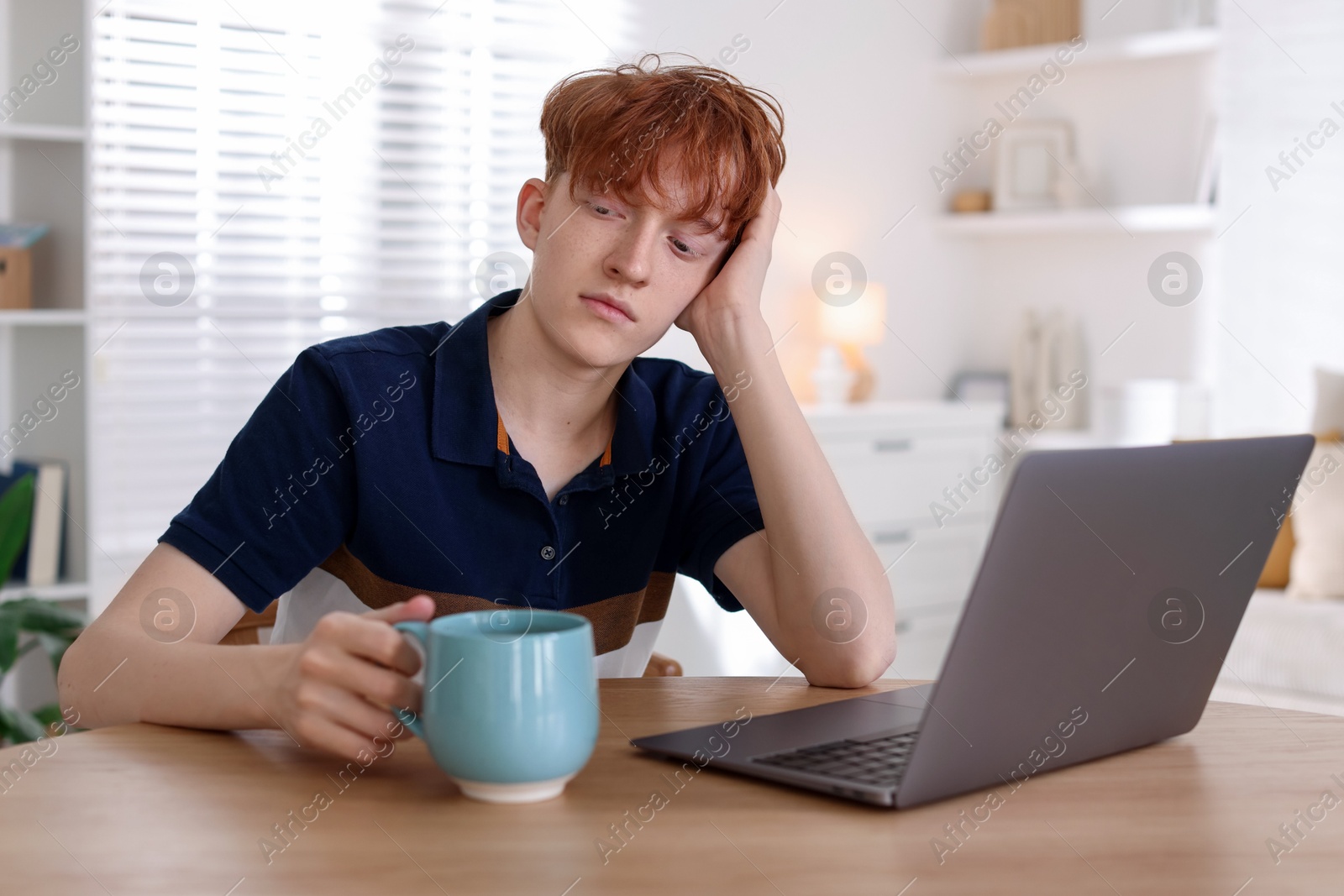 Teen problems. Depressed teenage boy with drink and laptop at desk indoors Photo of Teen problems. Depressed teenage boy with drink and laptop at desk indoors