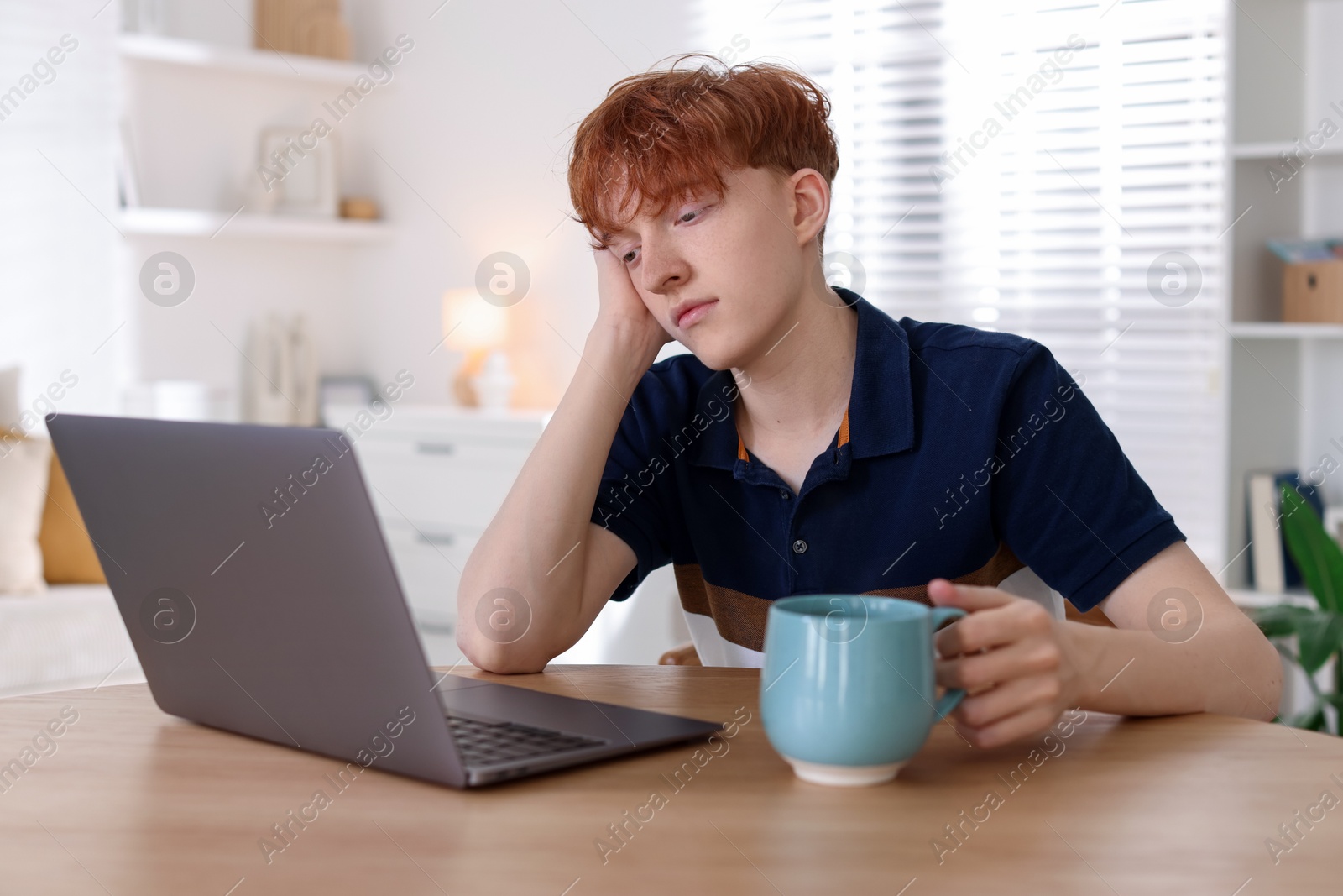 Teen problems. Depressed teenage boy with drink and laptop at desk indoors Photo of Teen problems. Depressed teenage boy with drink and laptop at desk indoors
