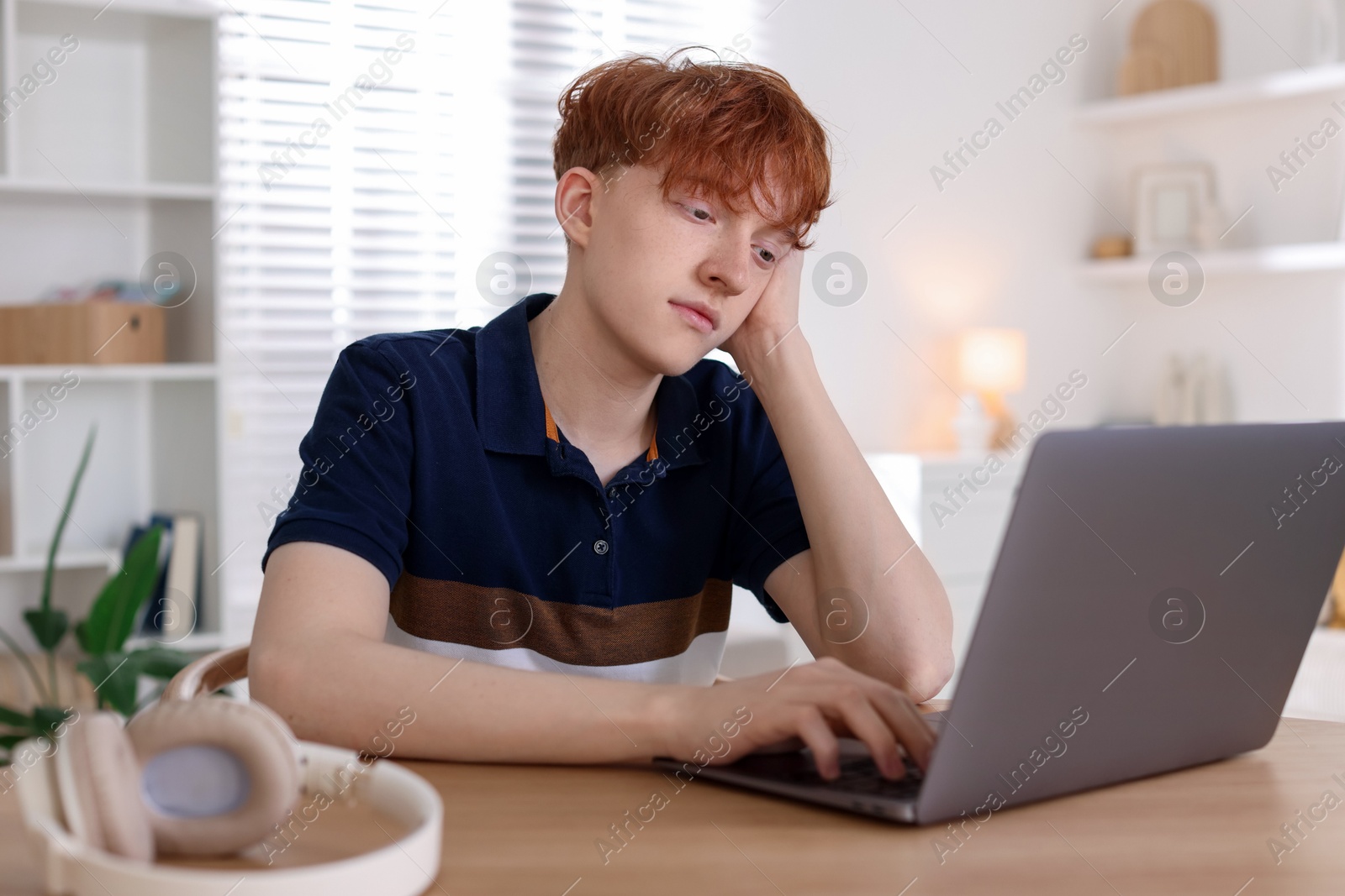 Teen problems. Depressed teenage boy with laptop at desk indoors Photo of Teen problems. Depressed teenage boy with laptop at desk indoors