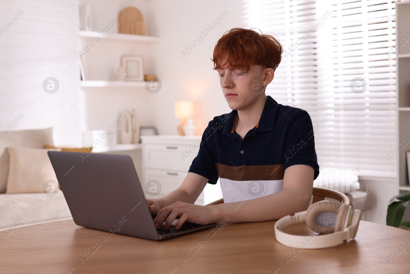Teen problems. Depressed teenage boy with laptop at desk indoors Photo of Teen problems. Depressed teenage boy with laptop at desk indoors