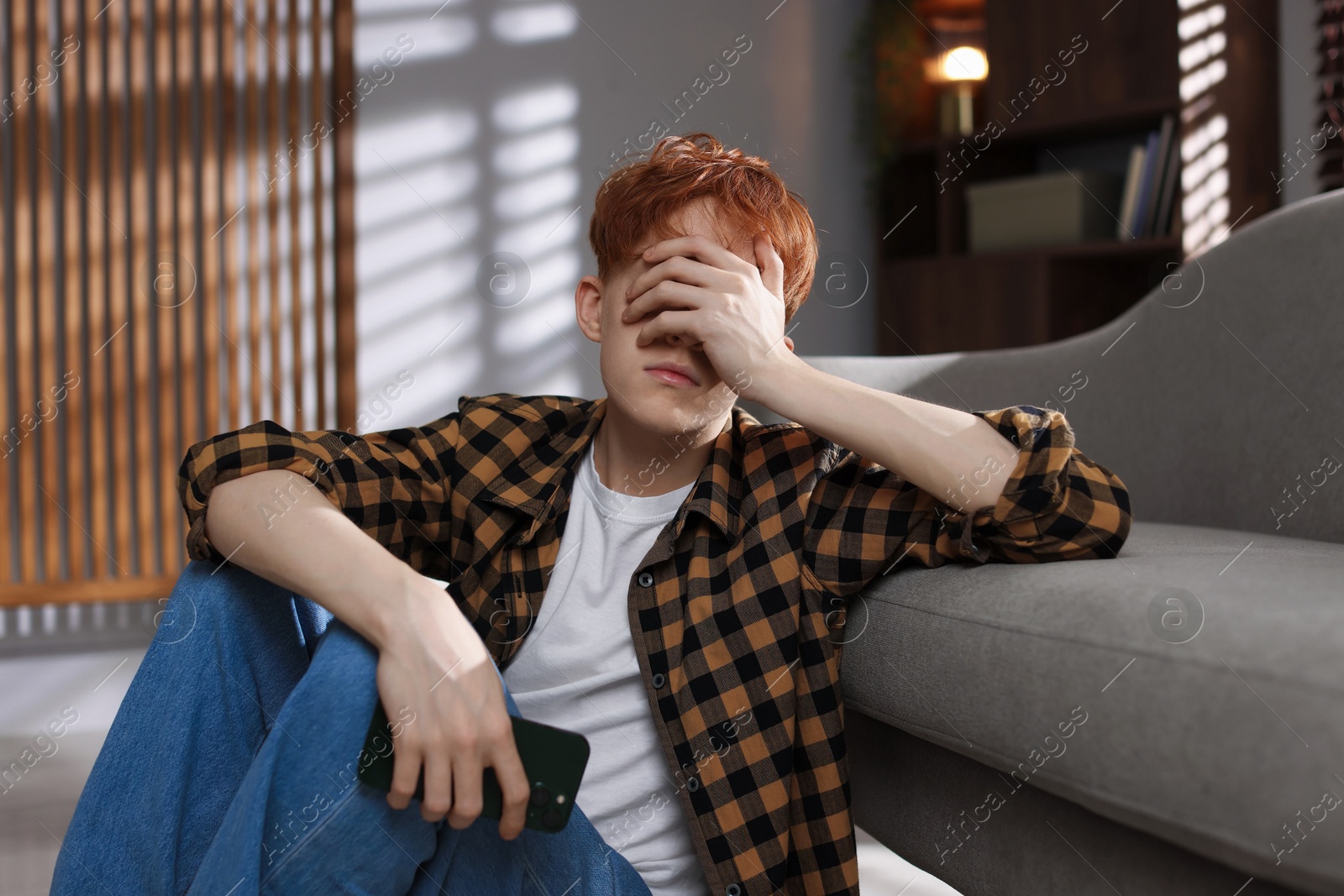 Teen problems. Depressed teenage boy with smartphone at home Photo of Teen problems. Depressed teenage boy with smartphone at home