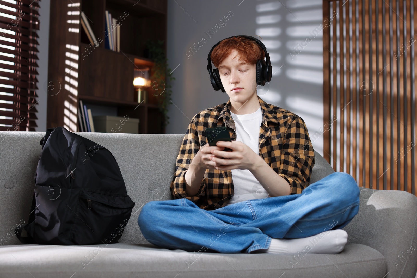 Teen problems. Depressed teenage boy with smartphone listening to music at home Photo of Teen problems. Depressed teenage boy with smartphone listening to music at home