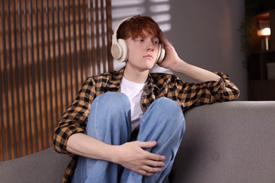 Photo of Teen problems. Depressed teenage boy listening to music on sofa at home