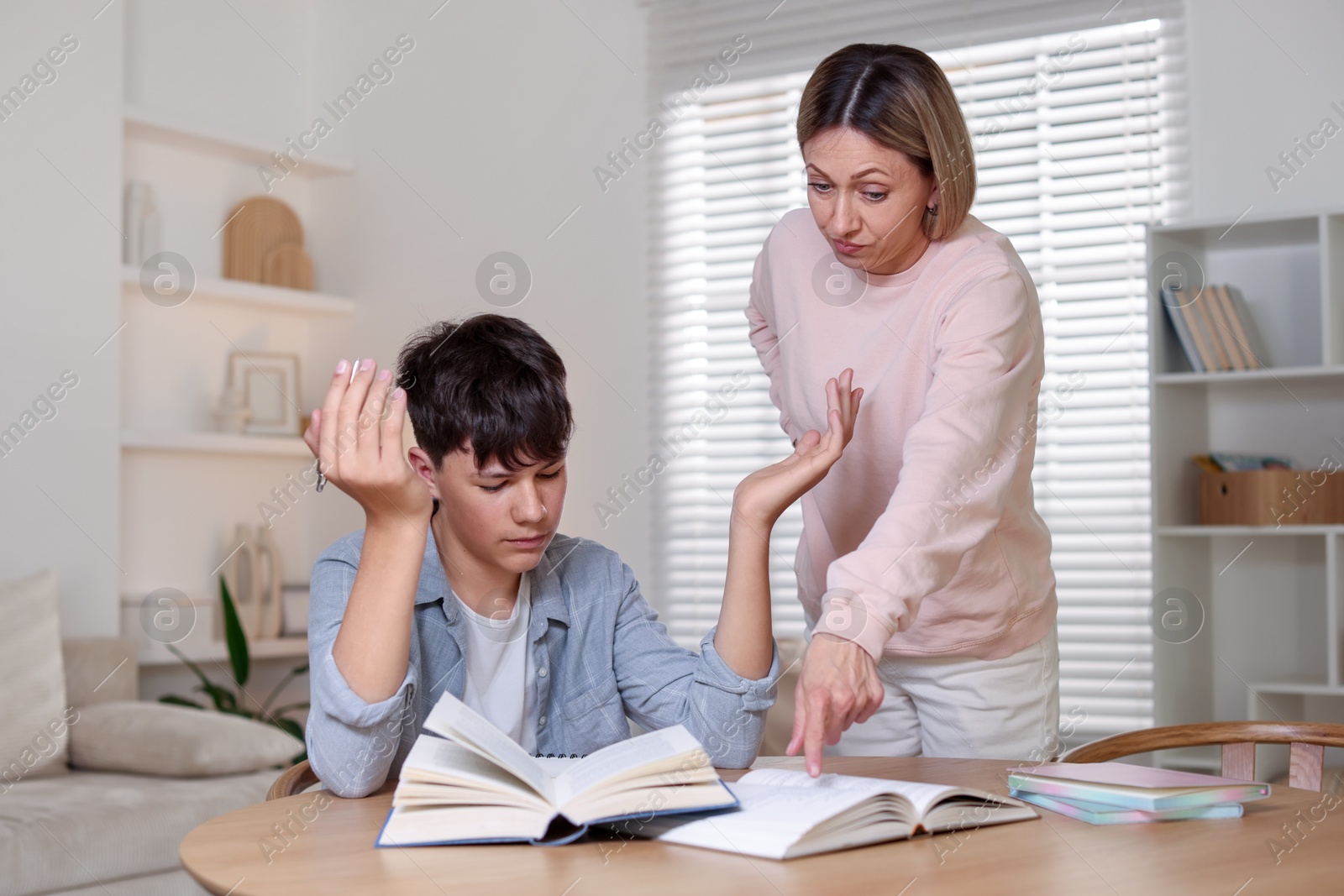 Annoyed mother and her stressful son doing homework at table indoors Photo of Annoyed mother and her stressful son doing homework at table indoors