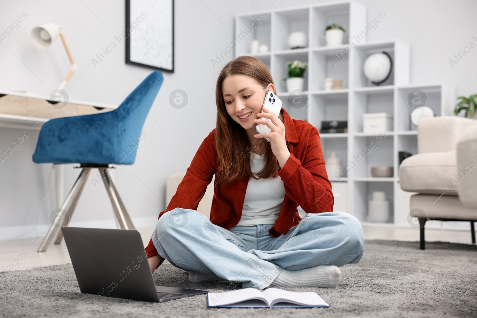 Teenage girl talking on smartphone near laptop at home Photo of Teenage girl talking on smartphone near laptop at home