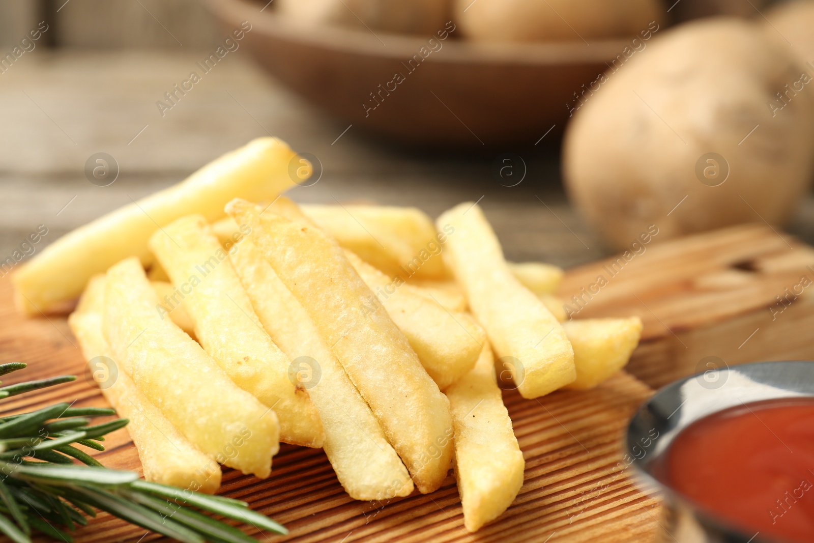 Photo of Tasty french fries served with ketchup and rosemary on wooden table, closeup