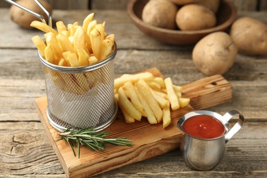 Photo of Tasty french fries served with ketchup and rosemary on wooden table, closeup