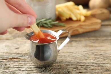Photo of Woman dipping french fry into ketchup at wooden table, closeup. Space for text