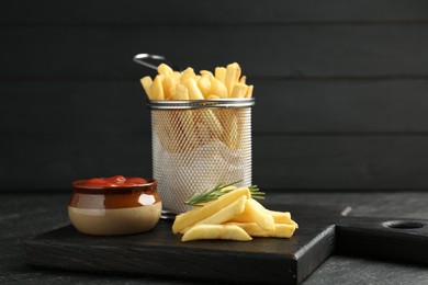 Photo of Tasty french fries served with ketchup and rosemary on black table, closeup