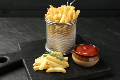 Photo of Tasty french fries served with ketchup and rosemary on black table, closeup