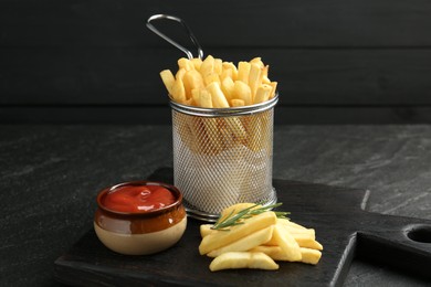 Photo of Tasty french fries served with ketchup and rosemary on black table, closeup