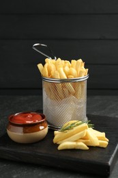 Photo of Tasty french fries served with ketchup and rosemary on black table, closeup