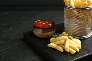 Photo of Tasty french fries served with ketchup and rosemary on black table, closeup. Space for text