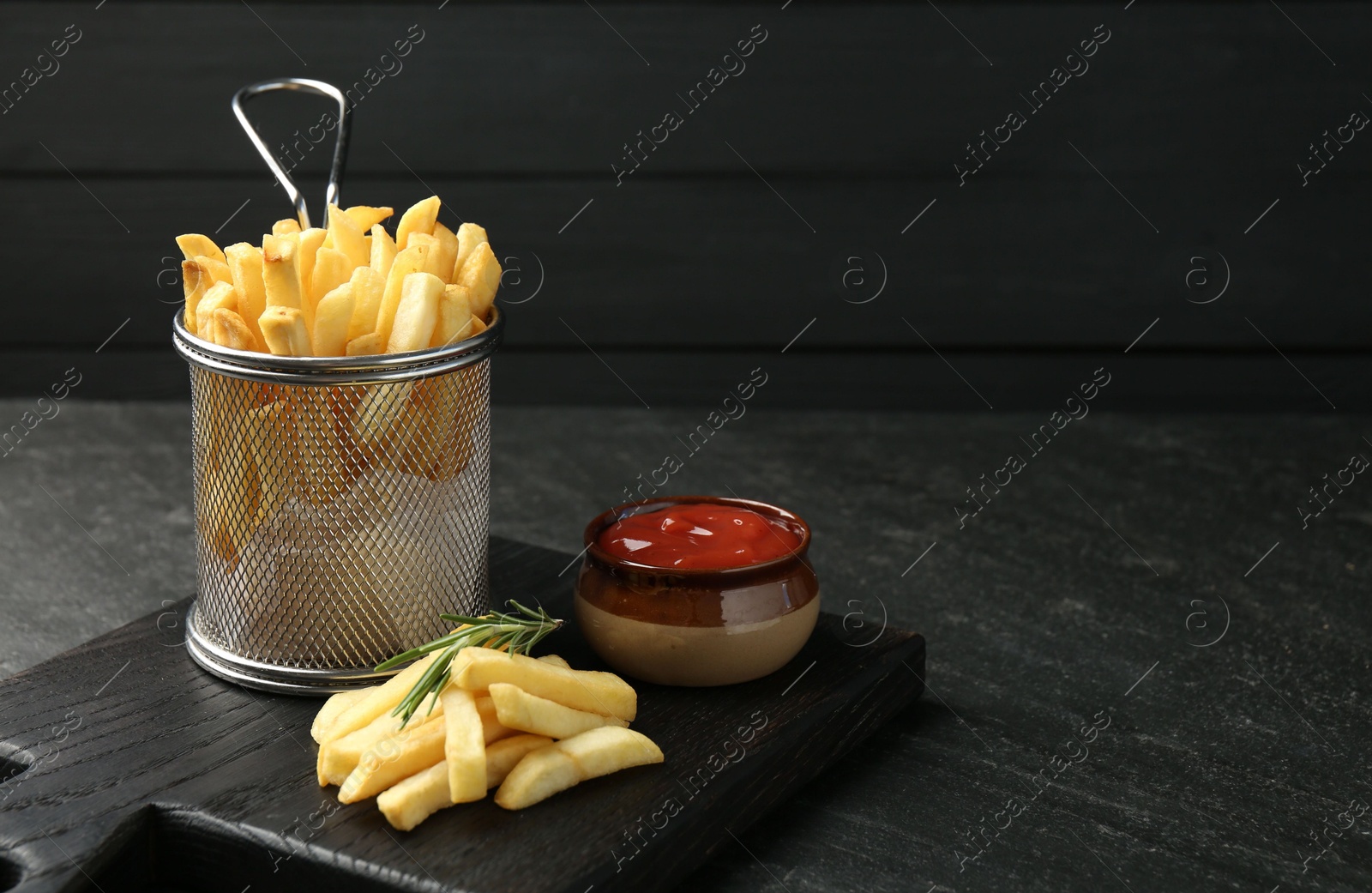 Photo of Tasty french fries served with ketchup and rosemary on black table, closeup. Space for text