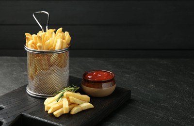 Photo of Tasty french fries served with ketchup and rosemary on black table, closeup. Space for text