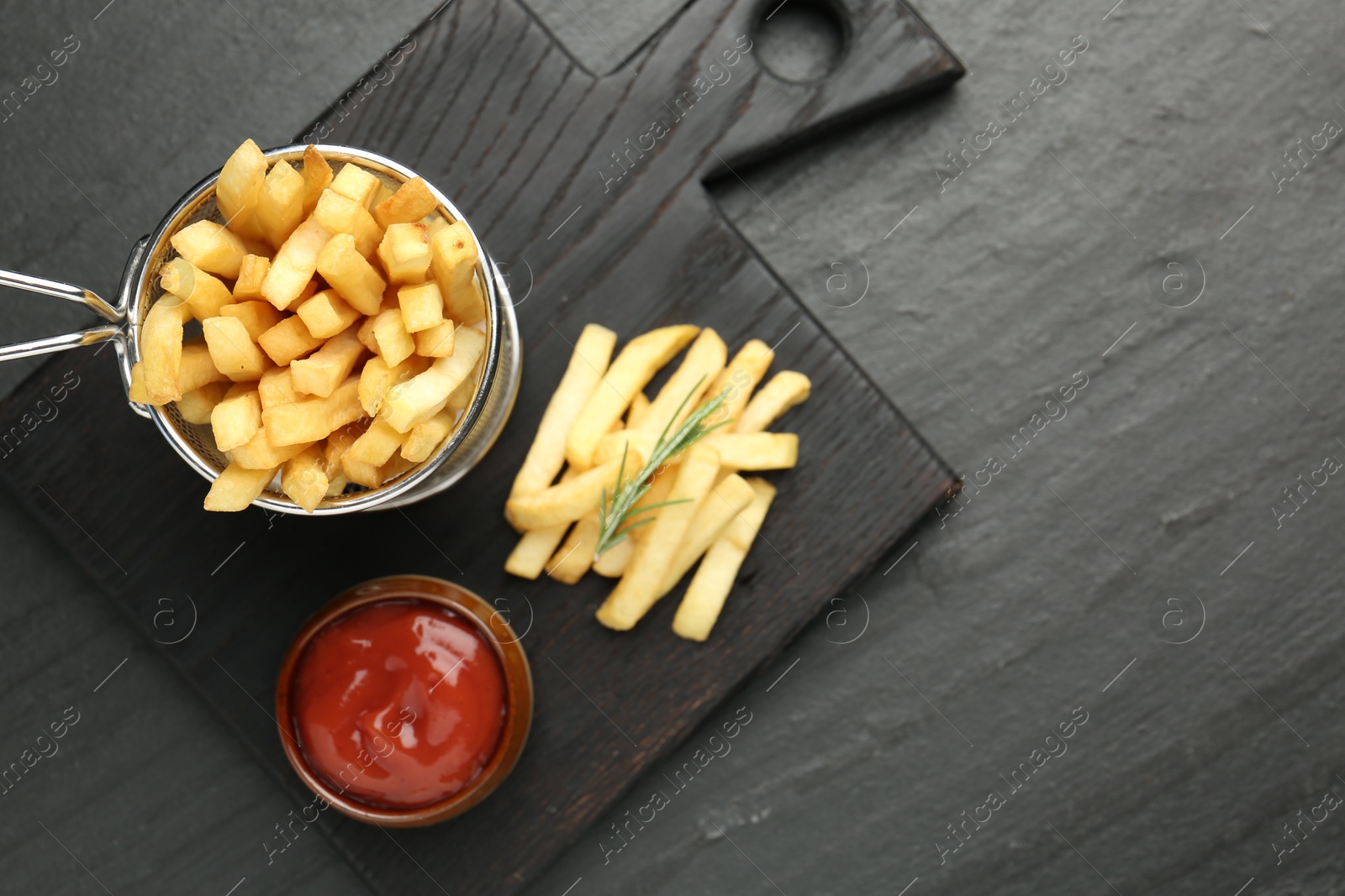 Photo of Tasty french fries served with ketchup and rosemary on black table, top view. Space for text