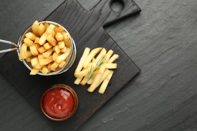 Photo of Tasty french fries served with ketchup and rosemary on black table, top view. Space for text
